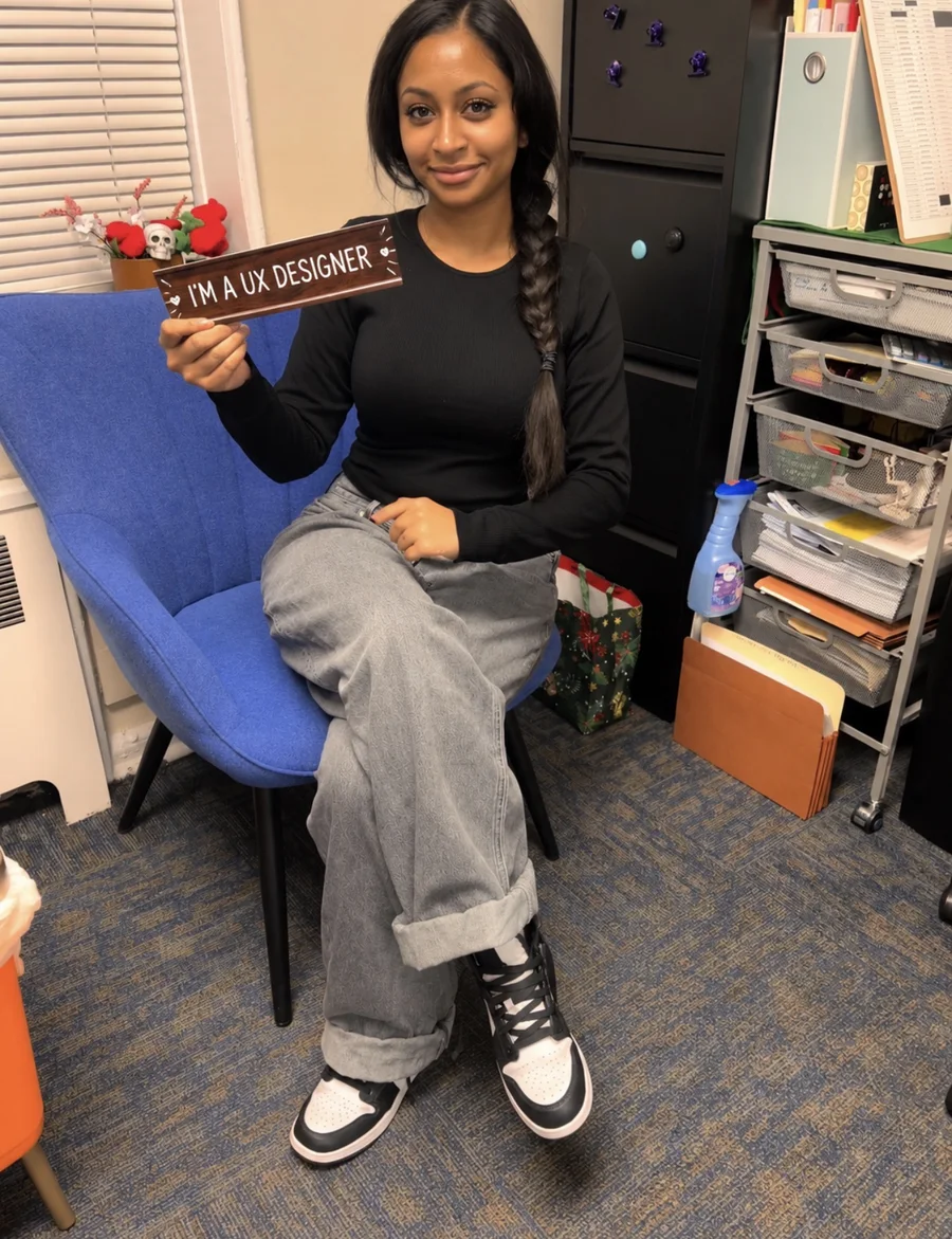 Shavanie in a blue chair holding a sign that says I’m a UX designer